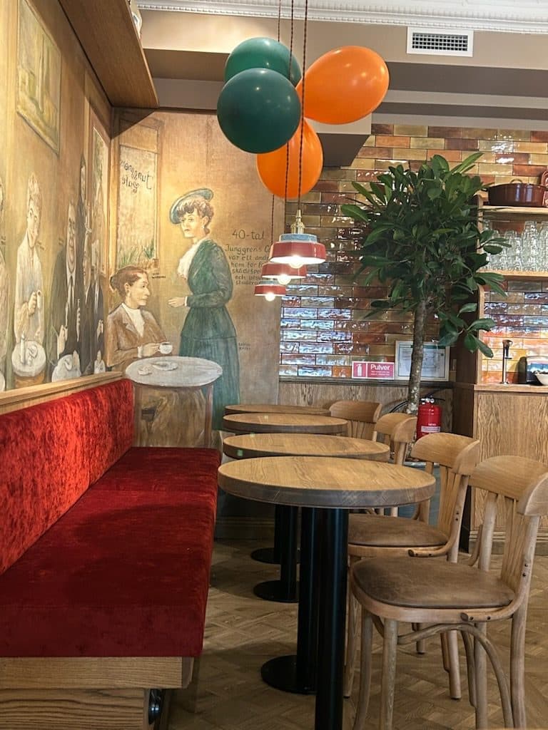 Färdigrenoverat kafé med röd sammetssoffa, träbord och bevarad väggmålning