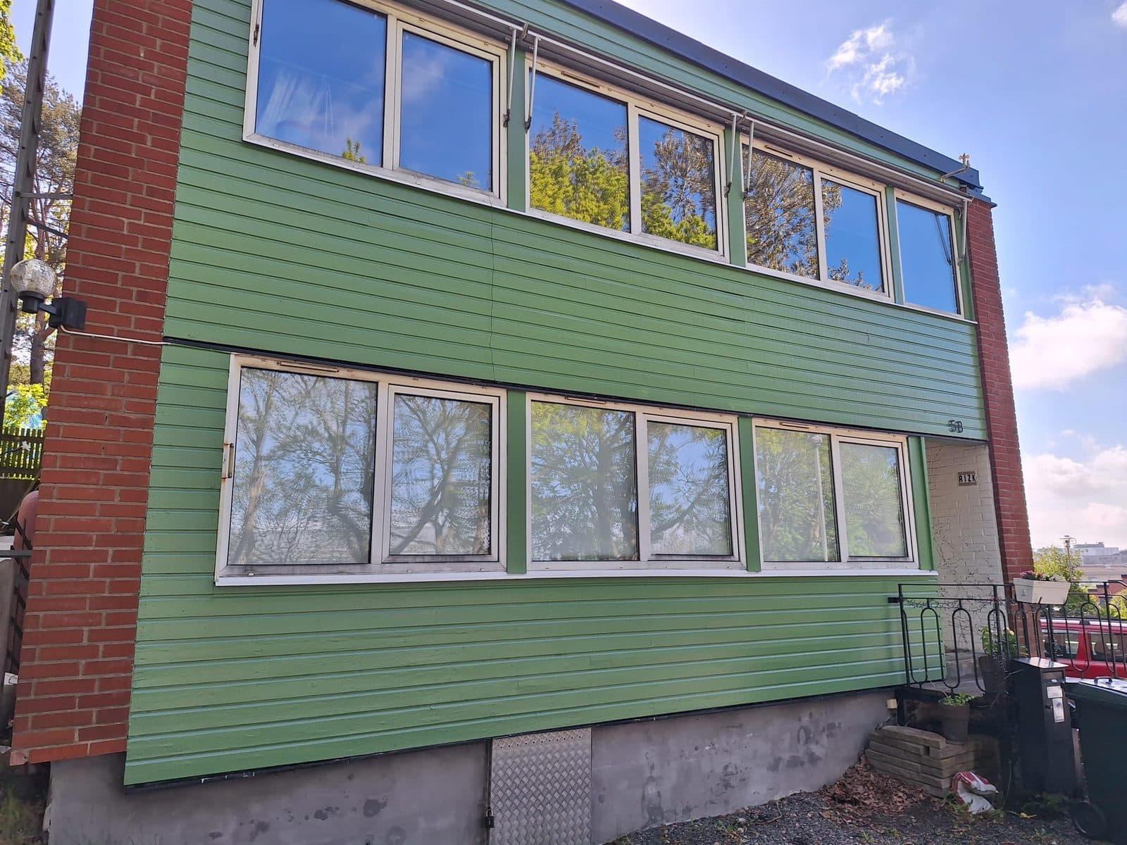 Nymålad grön träpanel med vita fönsterbågar på en villa med rött tegelparti